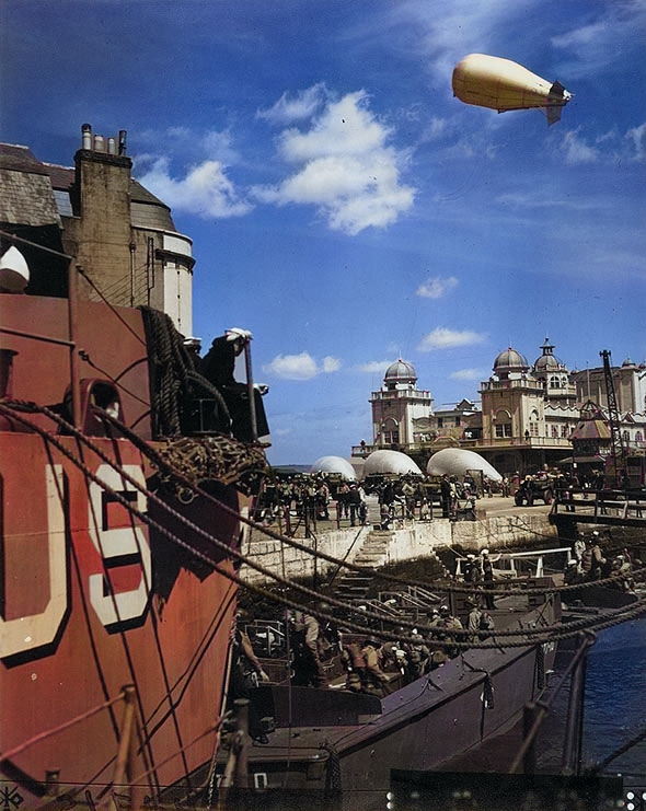 US Army soldiers boarding landing craft at Weymouth, Dorset, England, United Kingdom, while preparing for the Normandy operation, 1 May 1944; note barrage balloons aloft and on the ground [Colorized by WW2DB]