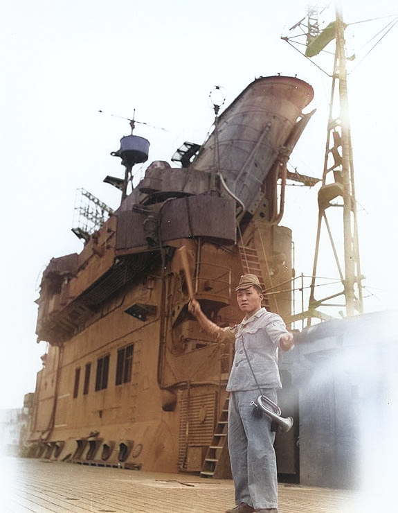 Japanese sailor aboard carrier Junyo signaling an approaching tug, Sasebo, Japan, 19 Oct 1945 [Colorized by WW2DB]