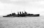 Cruiser HMS Cumberland underway in wartime disruptive paint scheme, 11 Mar 1942, location unknown. Note large aircraft hangar enclosure on the afterdeck.