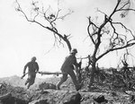 Two US Marines with an empty stretcher ran past a dead Japanese soldier, Iwo Jima, 3 Mar 1945