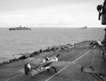 Grumman Martlet of 888 Squadron of British Fleet Air Arm taxiing on HMS Formidable after landing, circa 24 Apr-10 May 1942; HMS Warspite and AMC Alaunia in background