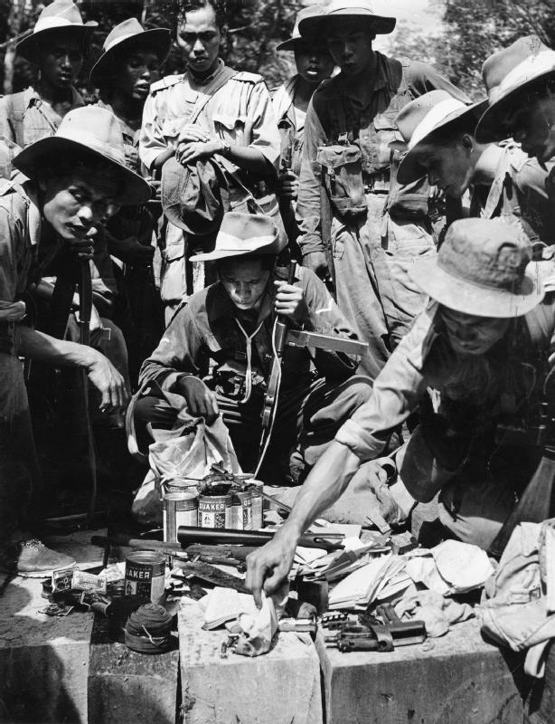 Troops of Malay Regiment inspecting captured communist equipment, Malaya, 1949; note Sten gun